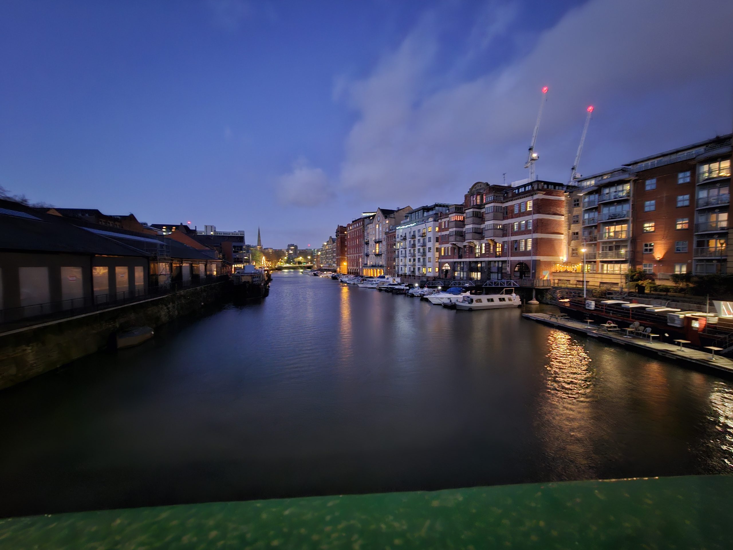 A beautiful night view of one of the Bristol canals, with shimmering lights reflecting on the water and a dark blue sky above.