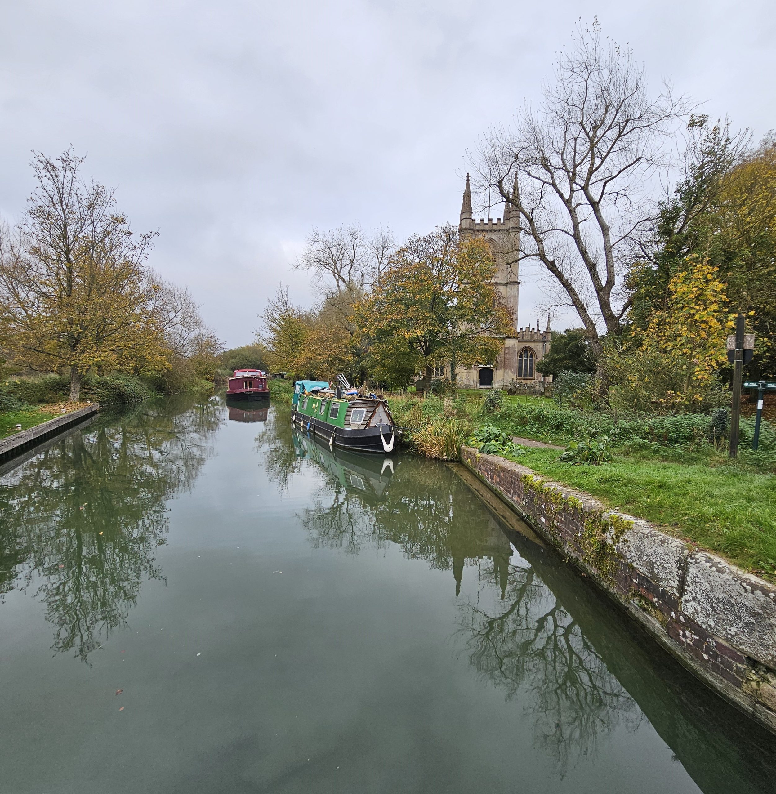 Scenic view of the Kennet and Avon Canal with St. Lawrence's Church in the background, framed by vibrant autumn foliage