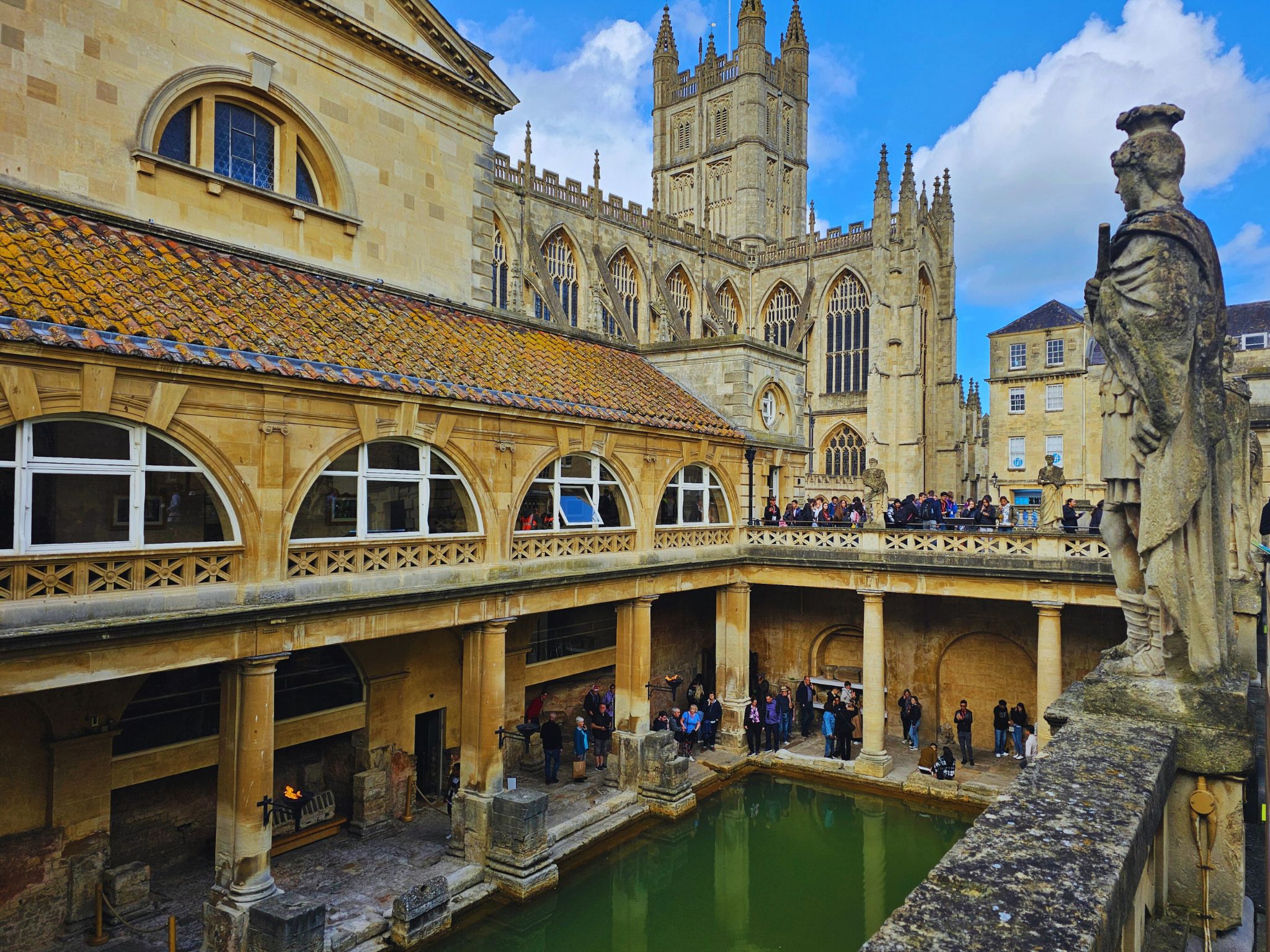 View of the Roman Baths from the first floor with the green Great Bath below and Bath Abbey rising in the backdrop.