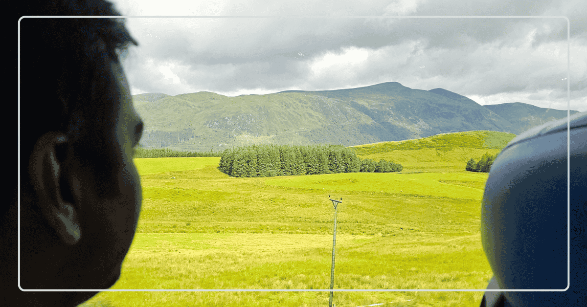 View of the Scottish Highlands through a train window with a passenger seated during the scenic rail journey from Glasgow to Fort William.